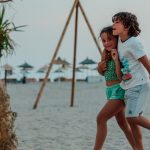Two children enjoy a playful walk on a sandy beach, capturing summer fun.