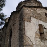 Low-angle view of an ancient stone building in Samos, Greece, surrounded by greenery.
