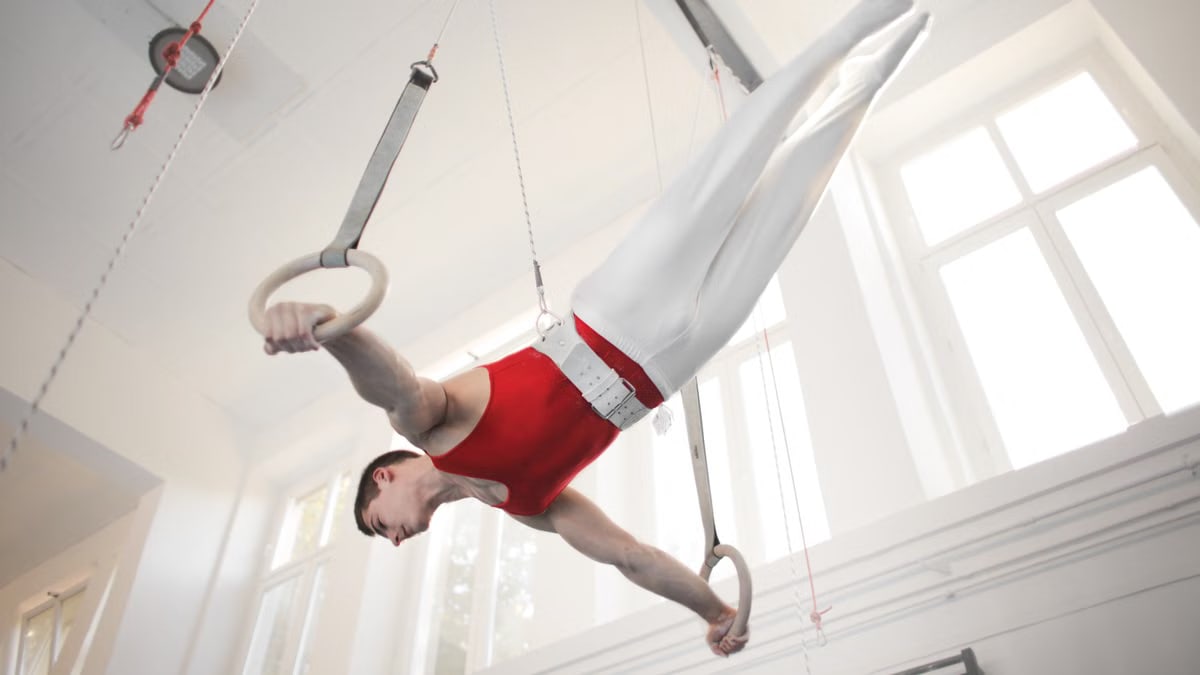 A male gymnast demonstrates strength and balance on rings indoors.